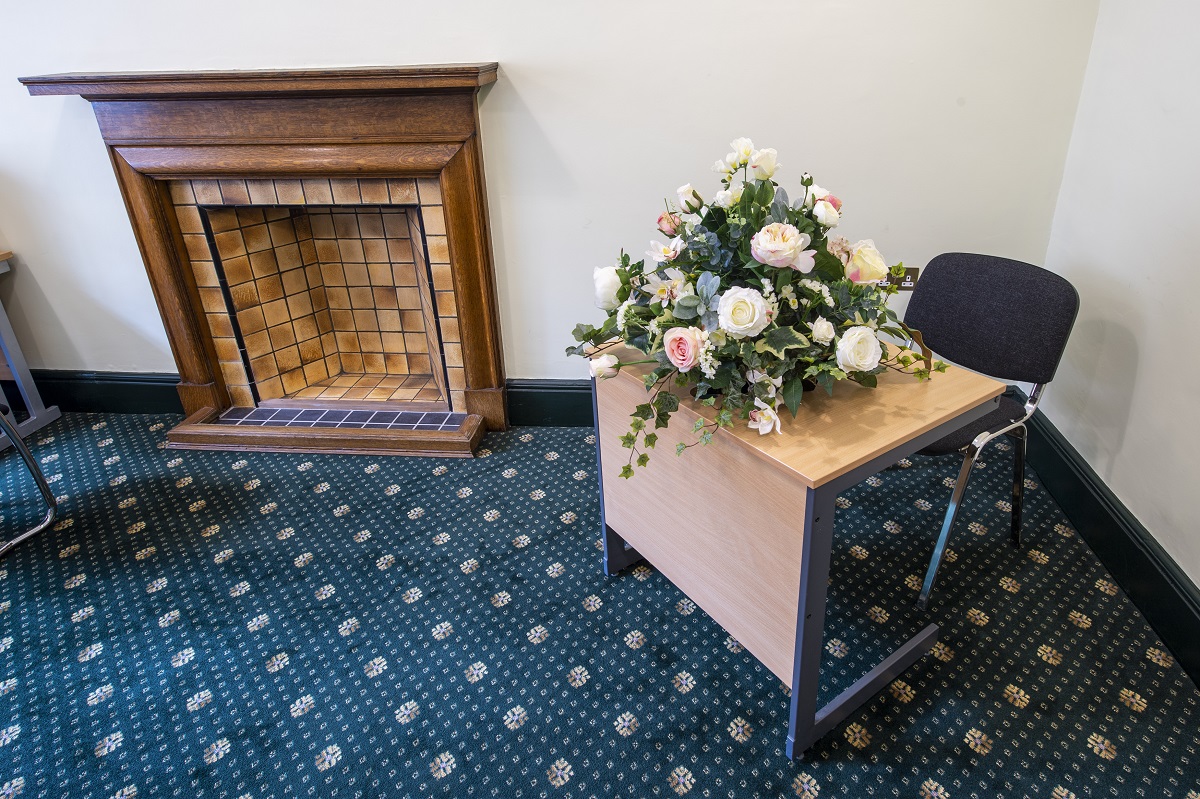 Small desk and chair with floral display and tiled fireplace in blue and pale pink room