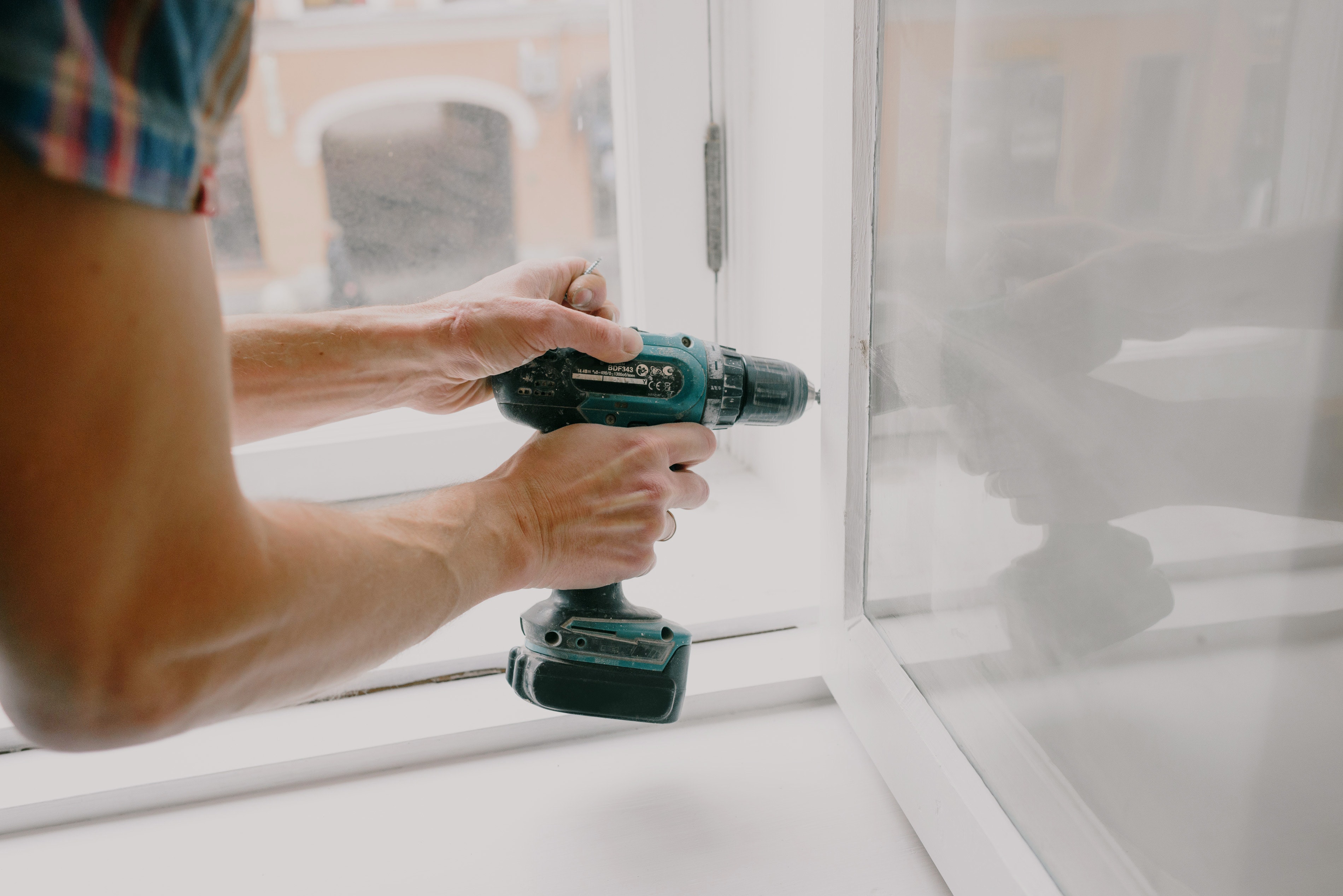 person holding electric drill to window hinge