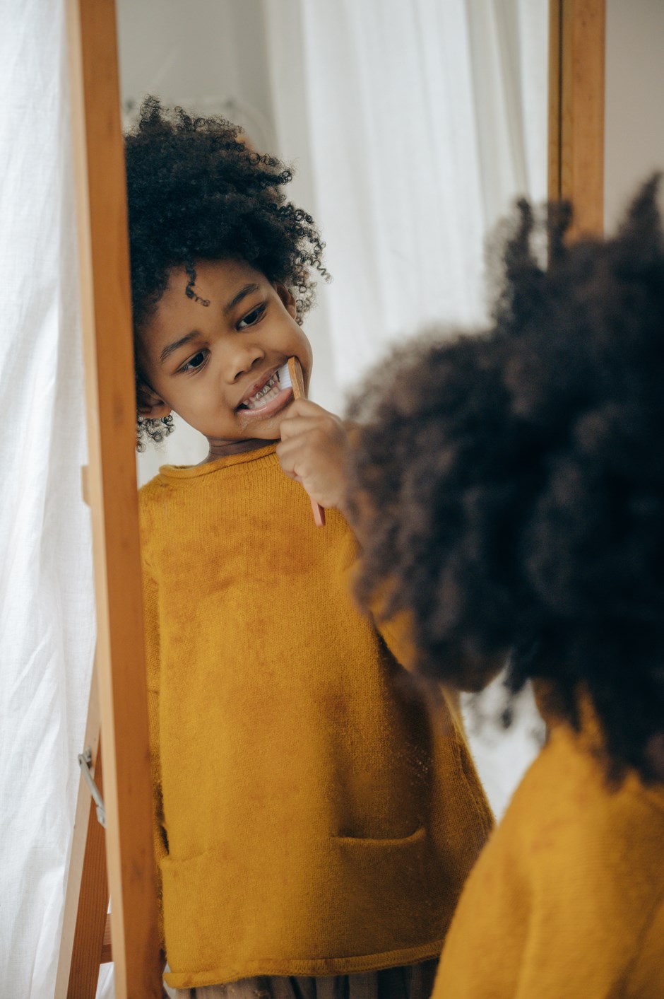 Child in a yellow jumper brushing their teeth in the mirror.