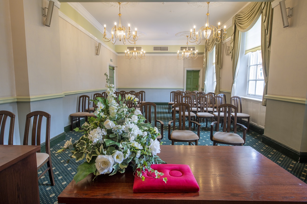 Large-sized room with blue and pale pink decor arranged for a ceremony with floral displays