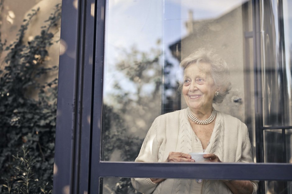 Smiling elderly woman looks out of her window
