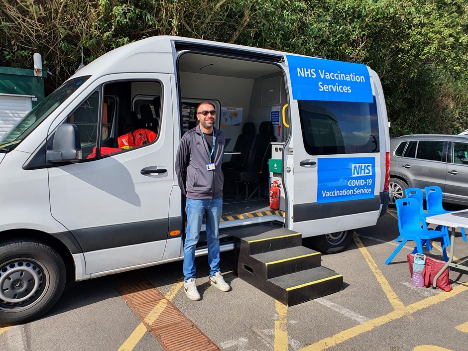 Male employee stood in front of NHS van with door open ready for patients